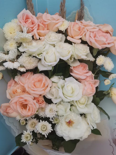 A floral arrangement featuring a bouquet of fresh roses in soft blush pink and creamy white, complemented by small white daisies and chrysanthemums. The flowers are arranged in a lush, natural style w