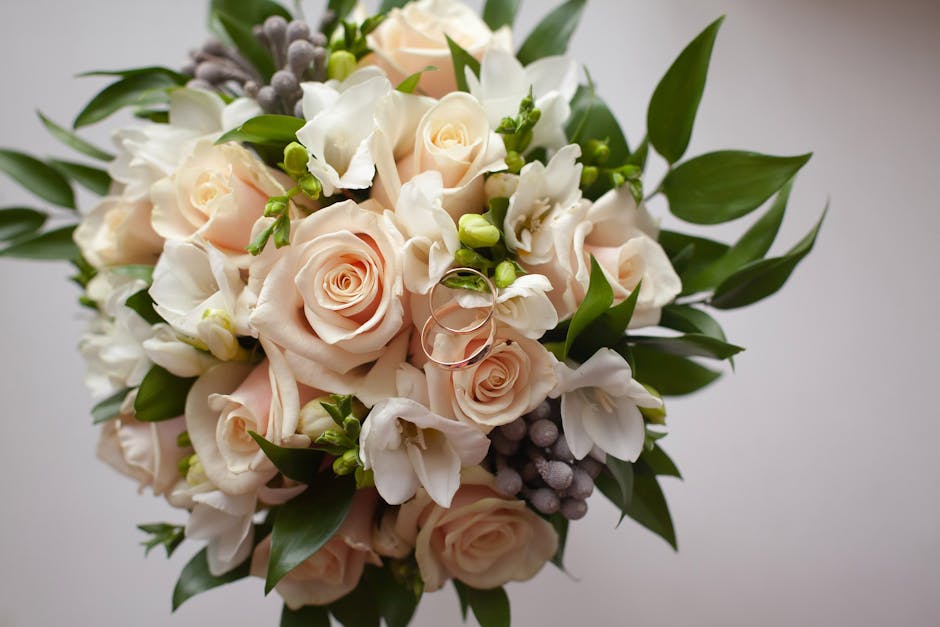 A close-up of a floral bouquet featuring pale pink roses with tightly layered petals, complemented by white freesias with delicate, trumpet-shaped blooms, and small clusters of grey berries. The arran